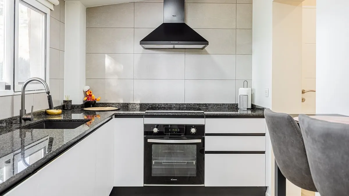Cozinha clara e moderna com forno embutido, coifa e bancada escura